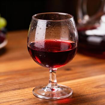 enfriado vaso lleno con oscuro rojo bebida descansa en un de madera superficie con condensación gotas foto