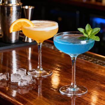 Two colorful chilled cocktails rest upon a highly polished wooden bar surface photo