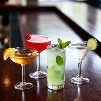 Assortment of four colorful mixed drinks rests attractively on a dark wooden bar surface photo