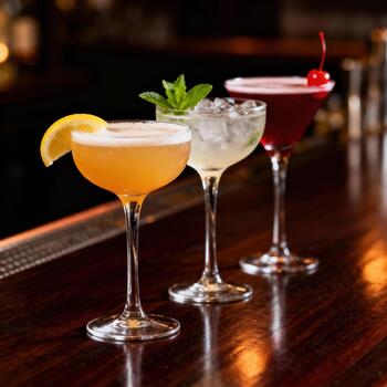 Tres distinto enfriado cócteles descanso en elegante copas sobre un pulido oscuro madera bar superficie foto