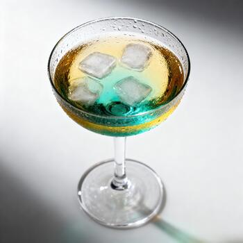 Chilled layered beverage with frozen cubes rests in a stemmed glass against a bright backdrop photo