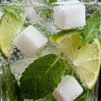 Close up view captures refreshing mixture of mint leaves, lime slices, sugar cubes, and carbonated liquid inside a glass container photo