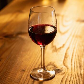 profundo rojo bebida descansa dentro un claro derivado vaso sobre un ricamente texturizado de madera superficie foto