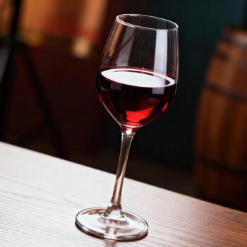 Glass filled with dark red beverage rests upon a wooden surface in a dimly lit environment photo