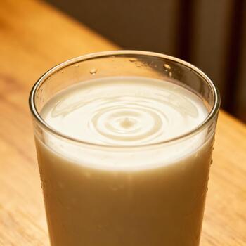 Frothy liquid settles in a clear glass atop a wooden surface with condensation visible. photo