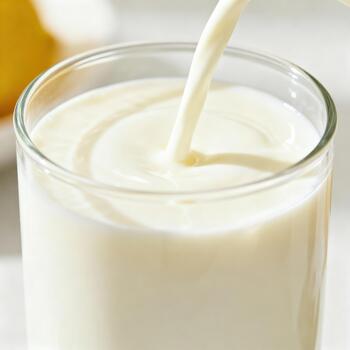 corriente de blanco líquido fluye dentro un claro vaso lleno con cremoso bebida foto