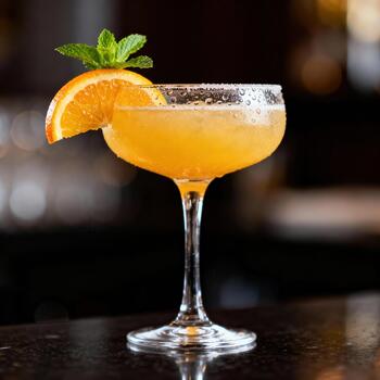 enfriado agrios bebida adornado con Fresco menta y un naranja rebanada descansa en un oscuro mostrador foto