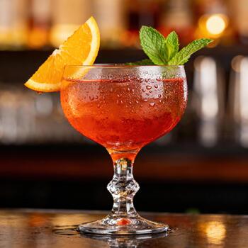 Refreshing chilled ruby colored beverage garnished with citrus fruit slice and fresh herb sprig rests on bar top photo