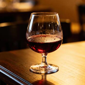 Deep red spirit rests in a stemmed glass on a warmly lit wooden surface photo