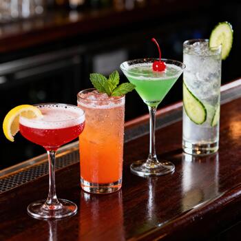 Four colorful, garnished mixed drinks rest upon a polished wooden bar surface photo