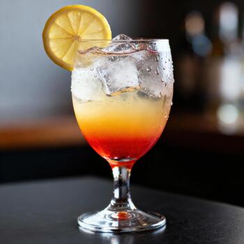 Chilled layered cocktail with citrus garnish sits on dark counter surface photo