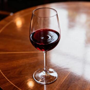 Goblet filled with deep ruby liquid rests upon a highly polished wooden surface. photo