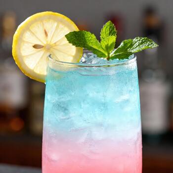 Tall glass containing a refreshing layered beverage garnished with citrus and fresh herbs photo