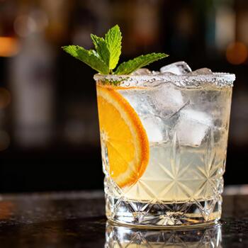 Chilled citrus beverage garnished with mint and served in a textured glass upon a dark counter photo