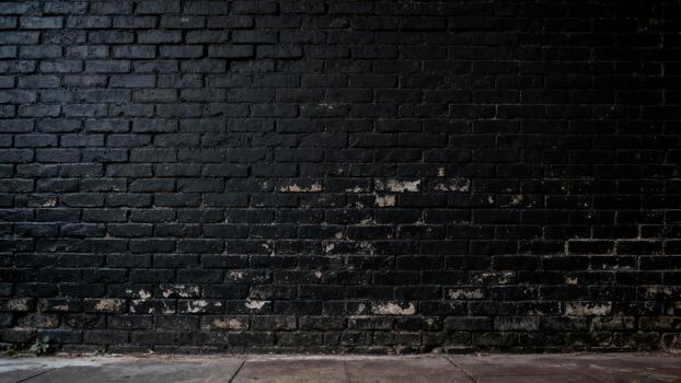 Weathered exterior brick surface is painted a dark matte color with peeling patches exposing lighter material underneath above a concrete pavement. photo