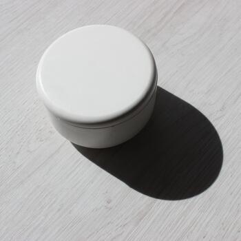 A deep shadow cast by a craft round caddy box standing on a wooden table square stock photo
