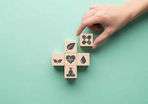 Hand placing a wooden cube with band aid icon on a cross of health and wellness blocks photo