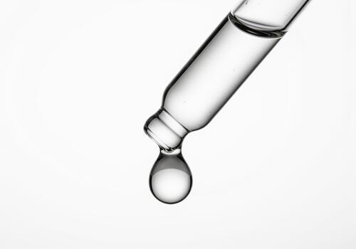 Precise clear liquid drop suspended from a glass dropper tip for science photo