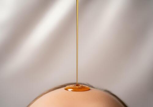 Continuous stream of golden oil flowing onto smooth skin surface photo
