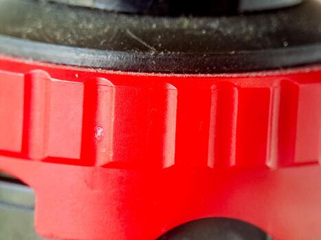 Fragment of a red mechanism with textured surface and a dark element above shows details. photo