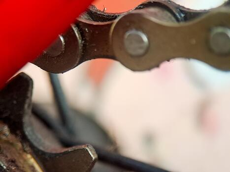 A gritty bicycle chain segment connected by pins and worn by friction against a red frame edge. photo