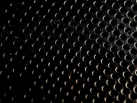The dark perforated surface showcases a repeating pattern of circular holes with gradient lighting. photo