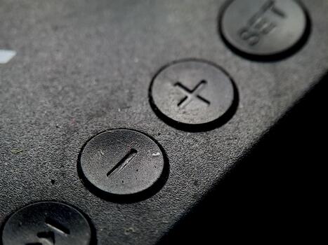 Textured black surface features round buttons with imprinted shapes, in dark and moody illumination. photo