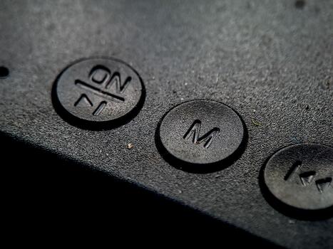 Textured black surface showing embossed controls with 'ON', 'M', and arrow icons in a dark mood. photo