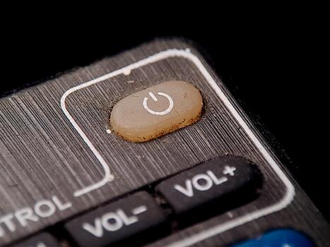 The power button on a remote control shows wear and age, sitting above the volume controls. photo