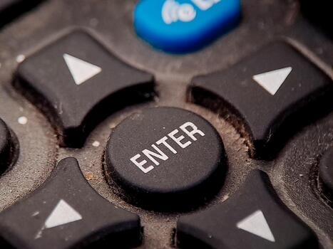 Macro shot of a well-used remote control, highlighting the 'Enter' button and navigation keys. photo