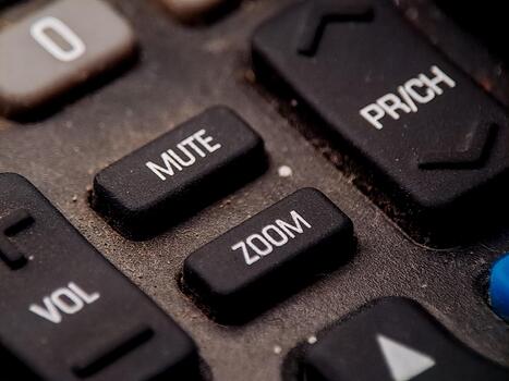 A macro shot highlights well-worn remote buttons, focusing on zoom and mute functionality for media. photo