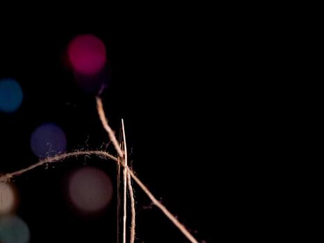 Needle and thread in the dark, illuminated by colorful bokeh creating an ethereal, dreamy mood. photo