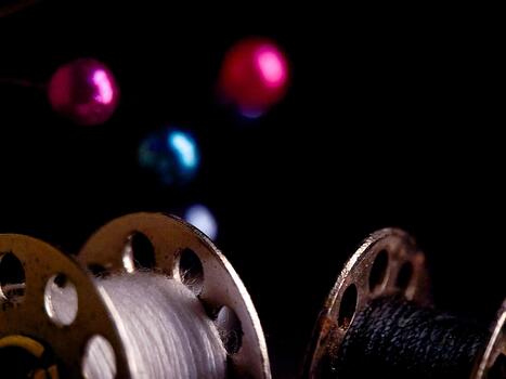 Evocative low-key photograph displaying spools of thread and sewing pins on a dark backdrop. photo