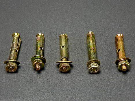 Five metal expansion bolts placed in a horizontal line on a textured gray surface, creating pattern. photo