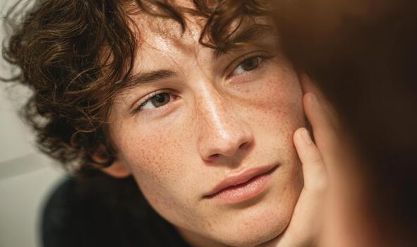 Young man observing reflection in mirror contemplating skincare photo