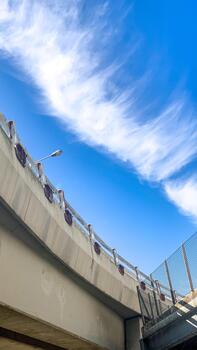 Bright blue sky and wispy clouds contrast with the concrete structure of the bridge, creating an interesting visual photo