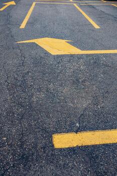 A close-up view of a parking lot surface with faded asphalt and yellow directional arrows. The ground shows wear and tear, indicating frequent use. photo