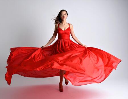 Woman in flowing red dress with elegant movement and confident expression on plain background photo