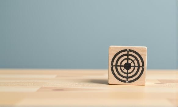 Wooden block with target symbol is placed on light wooden surface against blue background, creating minimalist and focused composition photo
