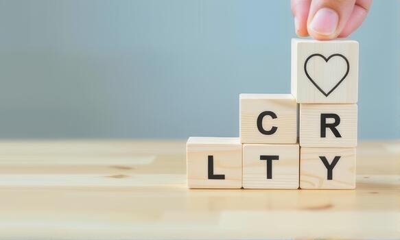 Wooden blocks stacked on table spell out CRLTY with heart symbol on top, symbolizing love and creativity. hand is placing heart block, adding personal touch to arrangement photo