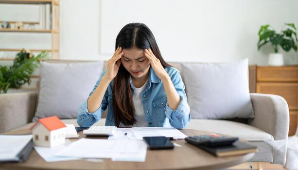 Woman with headache sitting at table with papers and calculator photo