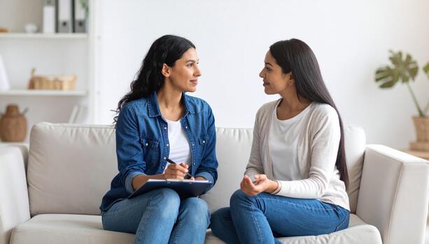 Empathetic conversation between two women on couch, sharing thoughts and ideas in cozy living room. atmosphere is warm and inviting, fostering connection and understanding photo