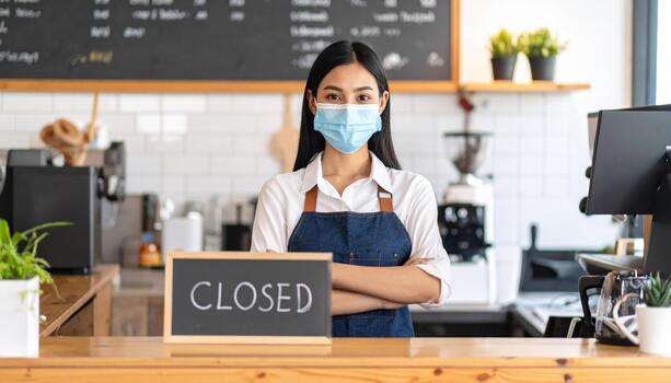 Young woman wearing mask stands behind counter in cafe, with CLOSED sign prominently displayed. atmosphere reflects moment of pause in bustling environment, highlighting impact of recent events photo