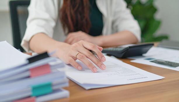Person is engaged in office work, with documents and calculator on wooden desk. scene conveys sense of professionalism and focus, highlighting importance of organization in workspace photo