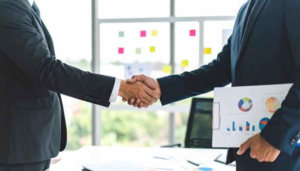 Business handshake agreement between two people in office with charts and graphs on paper, symbolizing partnership and success in bright workspace photo