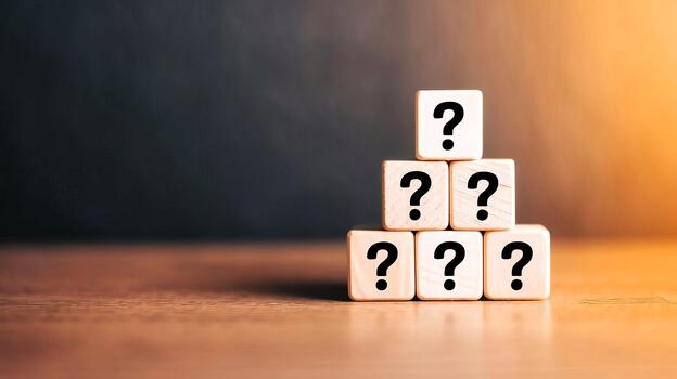 Stacked wooden blocks displaying question marks on a wooden table surface indoor photo