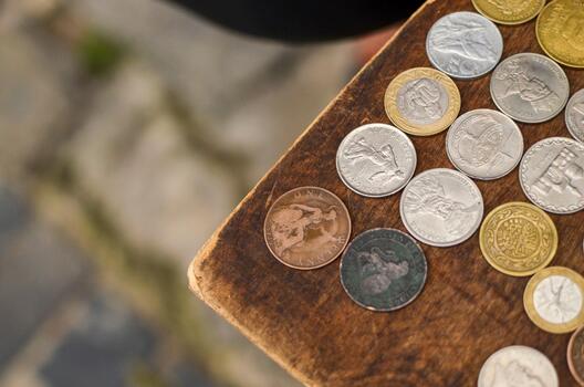 A collection of diverse coins, including gold, silver, and copper tones, are scattered on a rustic wooden surface, with a blurred background. photo