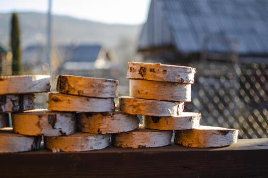 Stacks of round birch wood slices with visible bark rest on a wooden railing, against a blurred outdoor background. photo