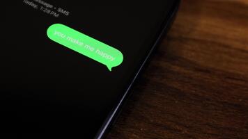 närbild se av en smartphone skärm som visar ett utgående du göra mig Lycklig text meddelande i en grön bubbla, fångad som den skickar med en slät dyka upp animation. video