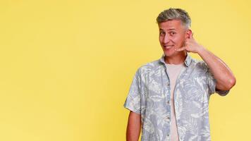 meia idade homem fazer ligar mim gesto perto orelha, então com confiança apontando para esquerda lado, convidativo para contato ou chamar, Claro intenção. cara expressando conexão solicitação isolado em amarelo fundo. video